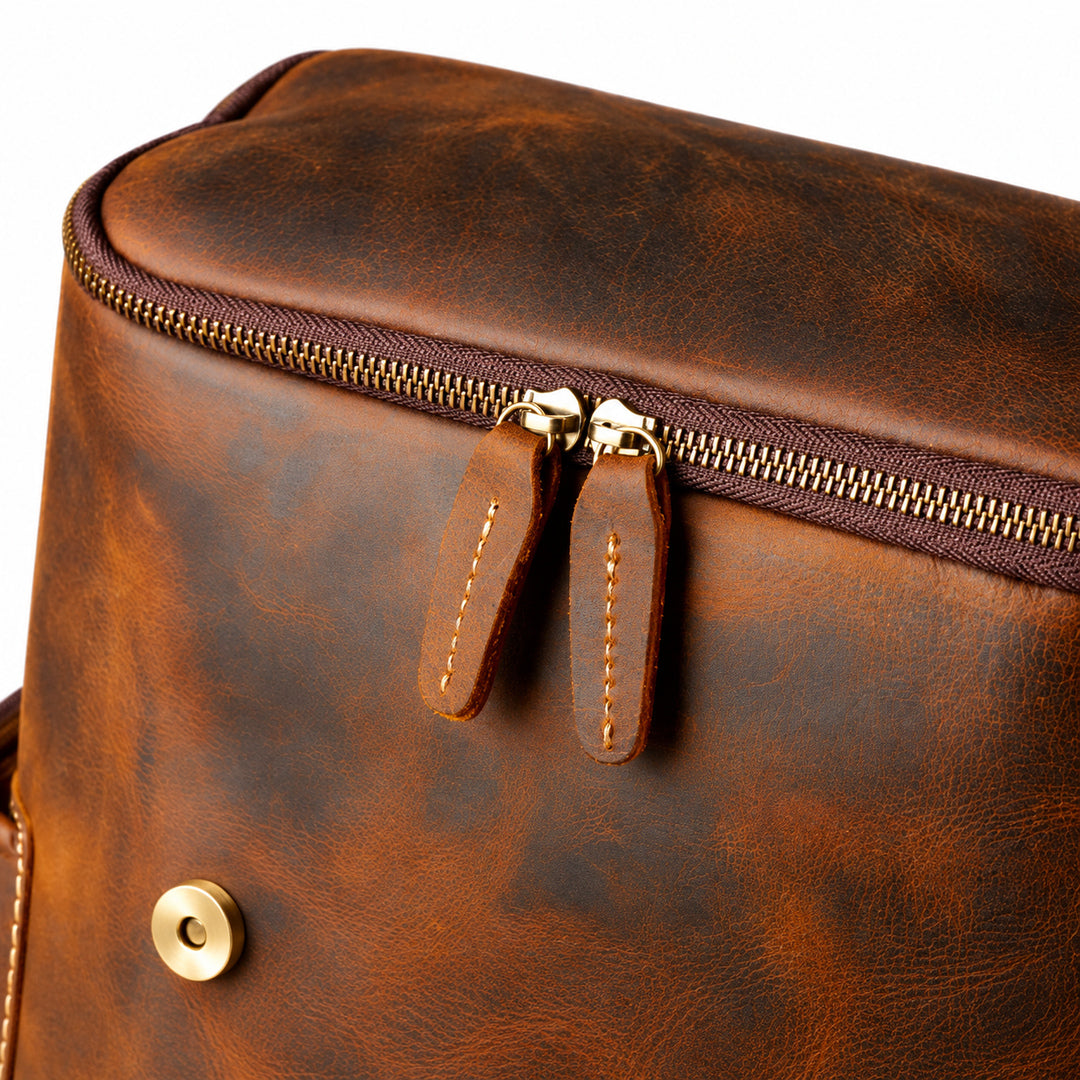 Close-up of a brown distressed leather bag with a top zipper, dual leather zipper pulls, and a brass snap button.