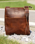 Brown Crazy Horse leather crossbody bag on gravel, featuring clean lines and detailed hand-stitching.