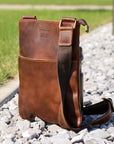 Brown Crazy Horse leather crossbody bag on gravel, emphasizing its durability and vintage style.