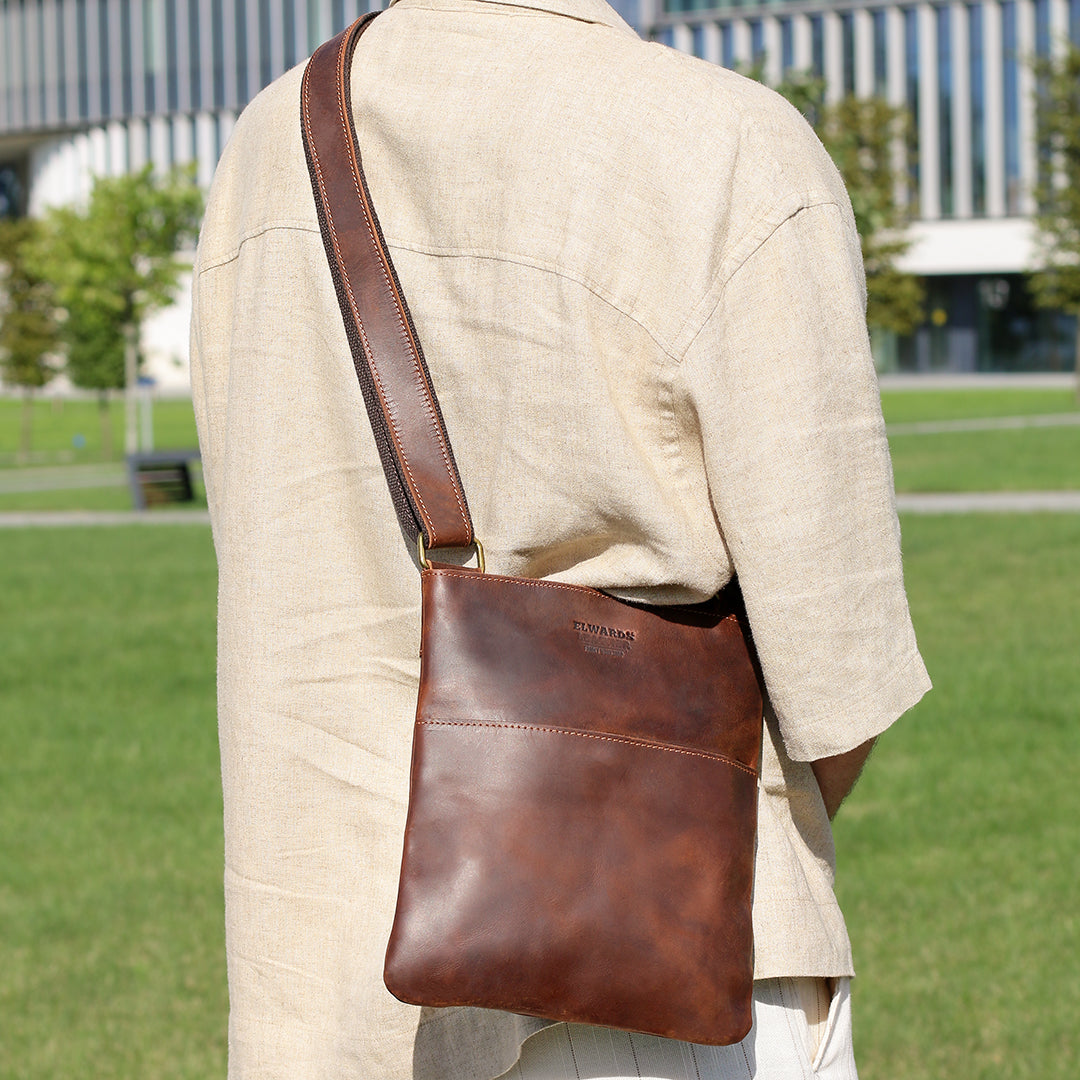 Man wearing a brown Crazy Horse leather crossbody bag on his back in a park, emphasizing its ergonomic and stylish design.