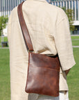 Man wearing a brown Crazy Horse leather crossbody bag on his back in a park, emphasizing its ergonomic and stylish design.