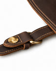 Close-up of a dark brown leather strap with tan stitching, a brass snap button, and a brass ring.