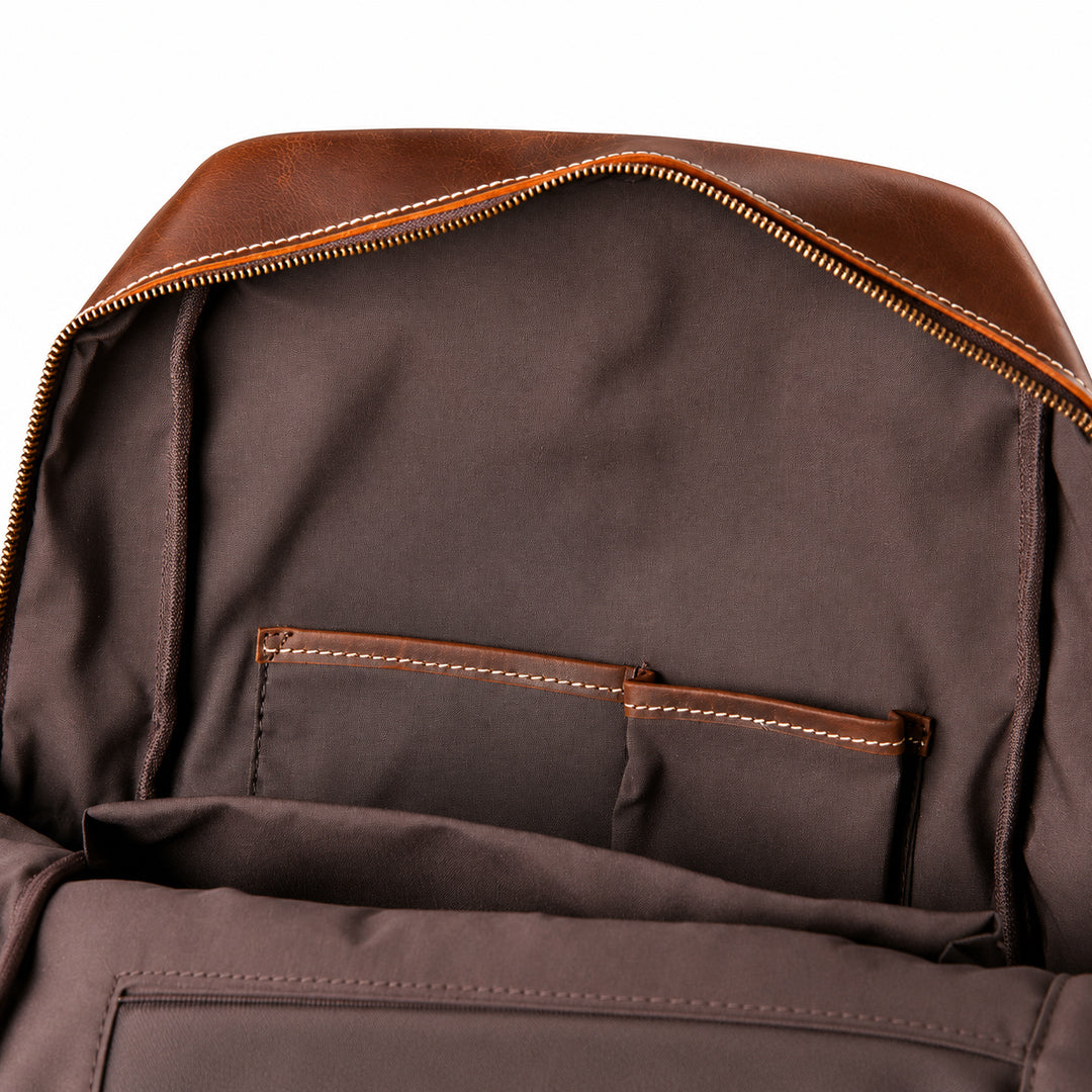 Close-up of the interior of a brown leather and fabric backpack, showing a zippered opening, interior pockets, and contrast stitching.