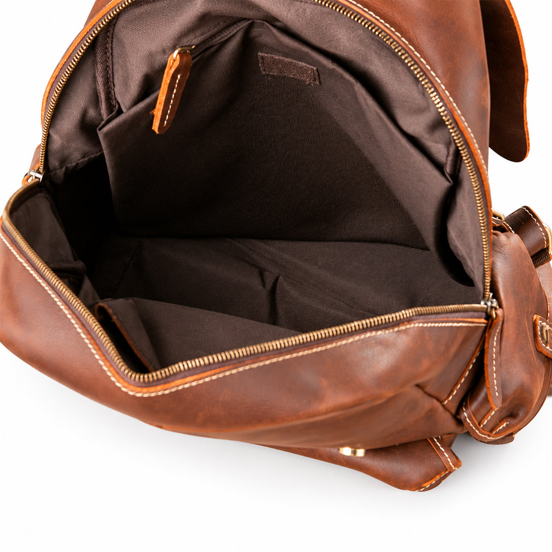 An open brown leather backpack or messenger bag showing the interior lining, gold-tone zippers, and stitching details.