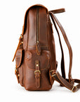 A brown leather backpack with a front flap pocket, zipper compartments, and adjustable shoulder straps.