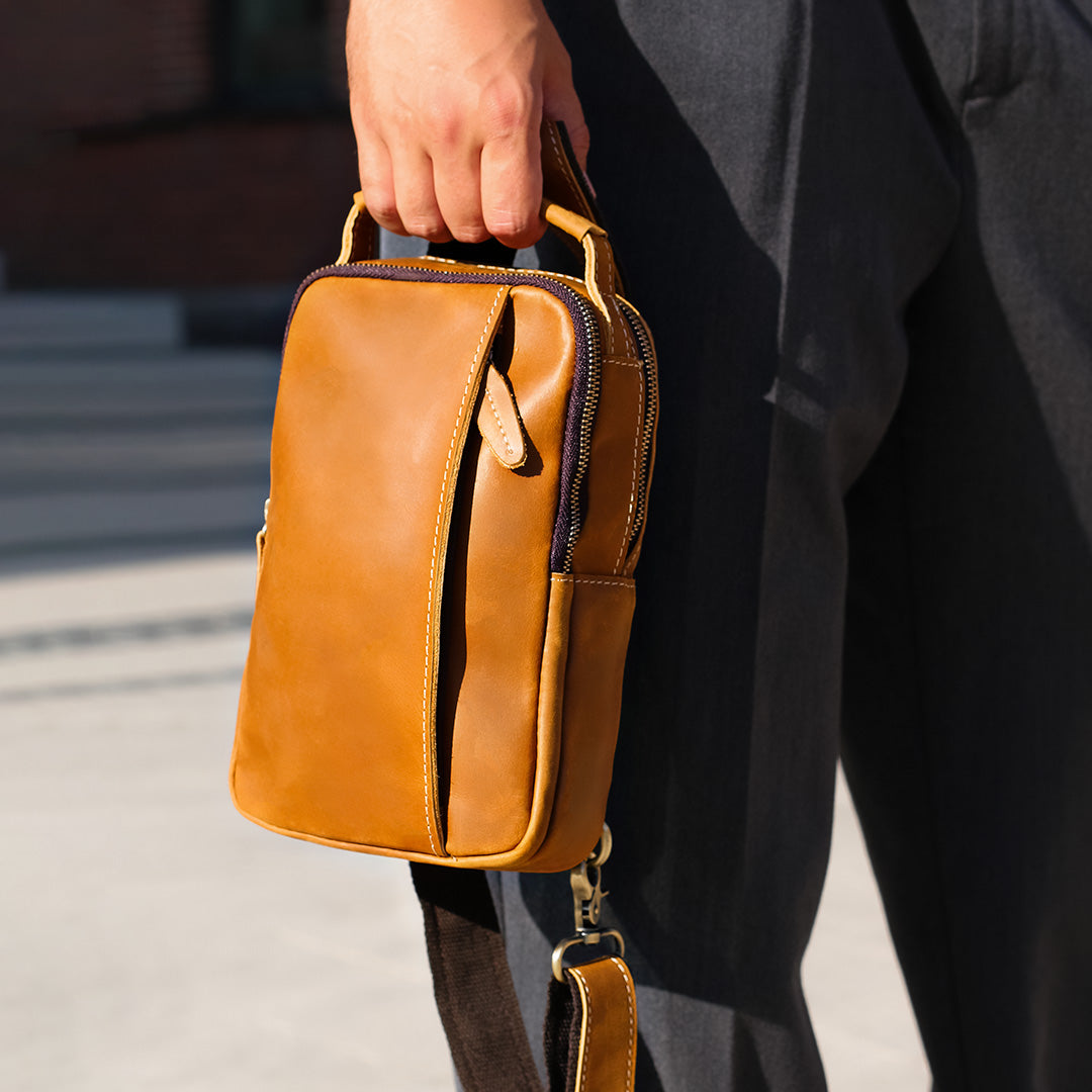 Brown leather sling bag carried in hand, durable and stylish everyday crossbody bag for men and travel