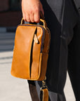 Brown leather sling bag carried in hand, durable and stylish everyday crossbody bag for men and travel