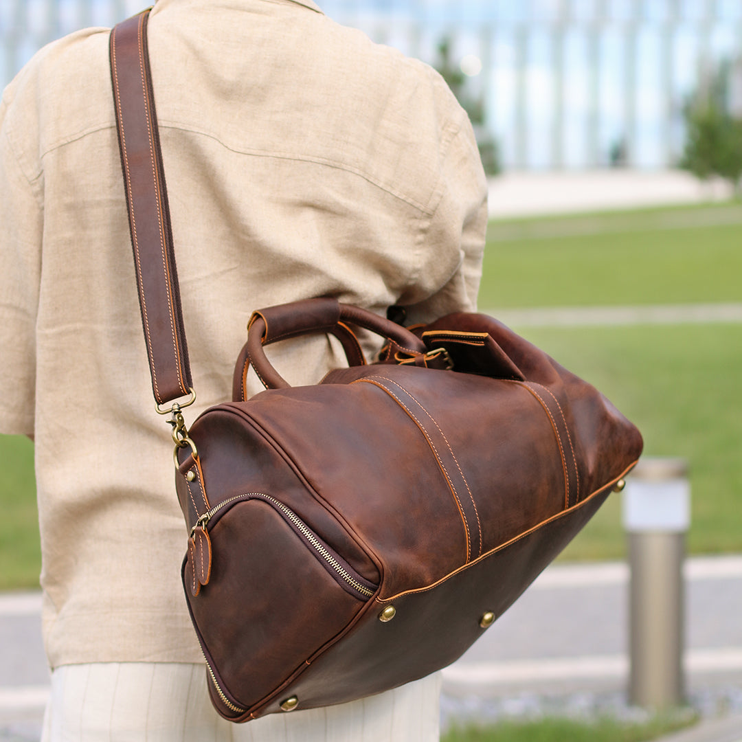 Stylish brown leather weekender bag with adjustable strap shown on shoulder outdoors.