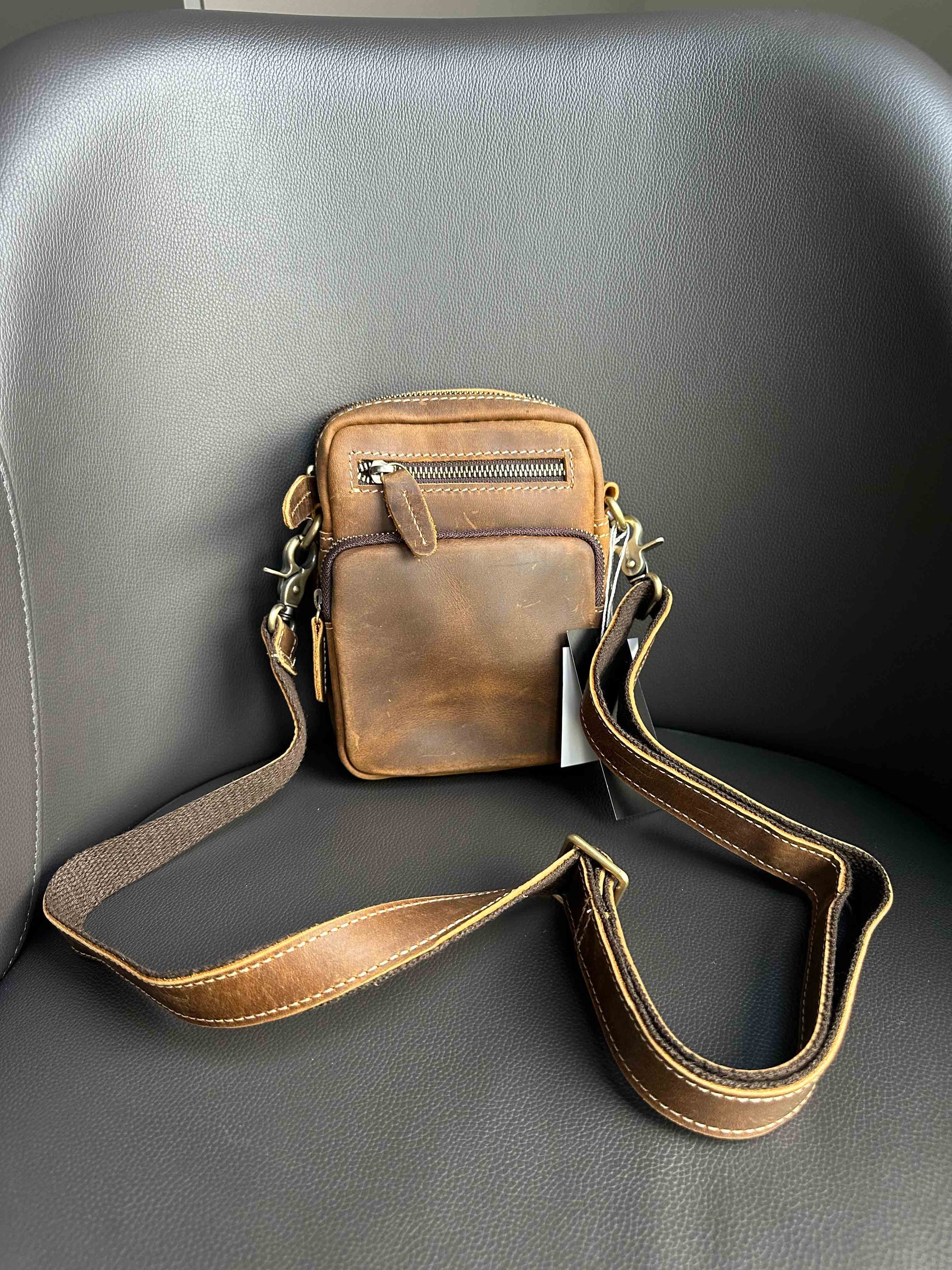 Brown leather crossbody bag on a gray chair