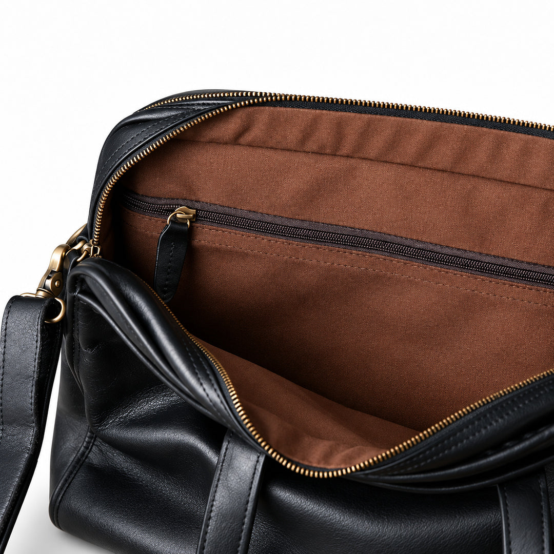 A close-up inside the black leather briefcase shows a horizontal zip pocket with a leather pull against brown lining.