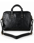 A black leather briefcase is shown with its detachable shoulder strap laid out to reveal the wide padded center and adjustable ends.