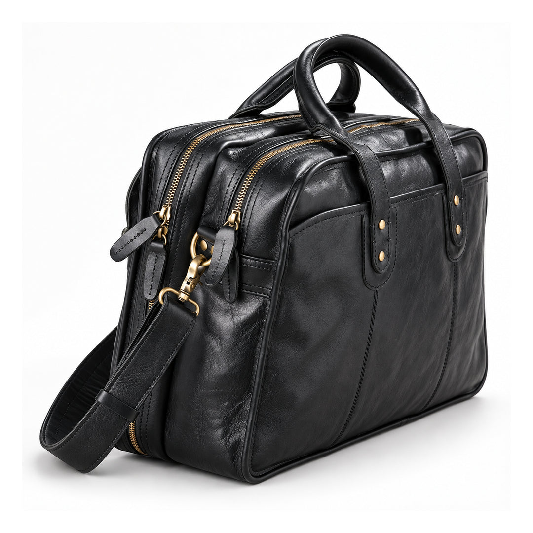 A black leather briefcase is shown at a side angle with twin zip compartments, leather zipper pulls and a brass-tone strap clasp.