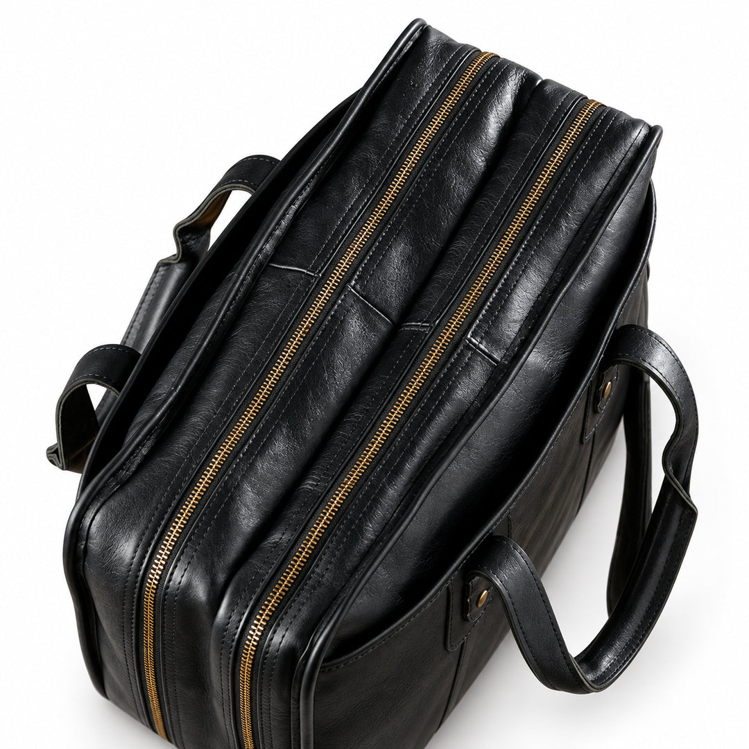 A top view of the black leather briefcase shows two parallel brass-tone zippers and folded carry handles.