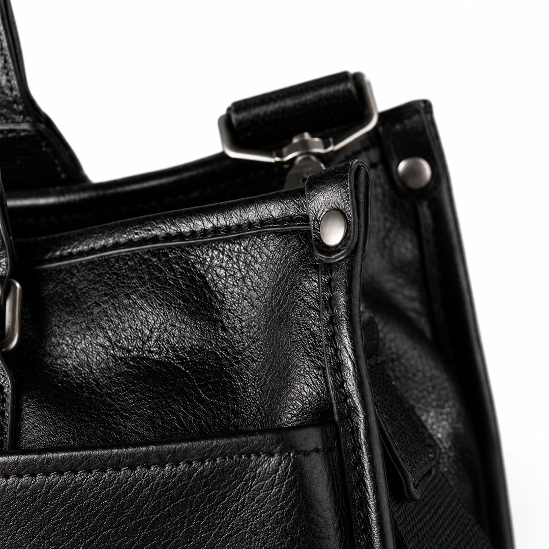 Classic black full-grain leather tote corner with a metal rivet, piped edge and strap attachment