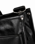 Classic black full-grain leather tote corner with a metal rivet, piped edge and strap attachment
