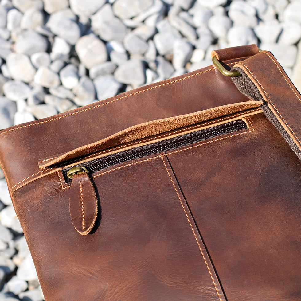 Close-up of a zipper pocket on a brown leather crossbody bag.