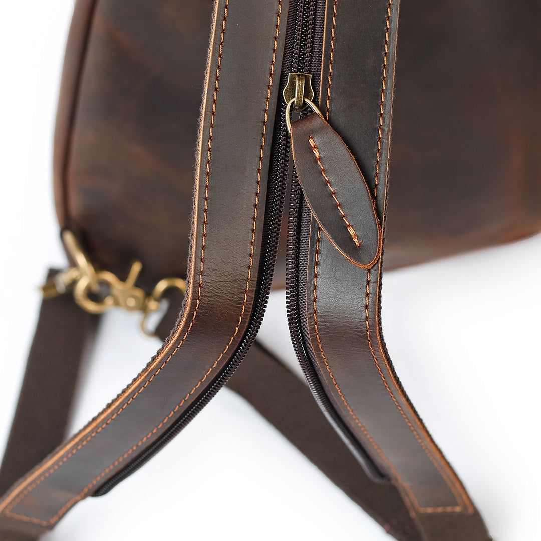 Close-up of a brown leather bag with gold zipper pull on a white background
