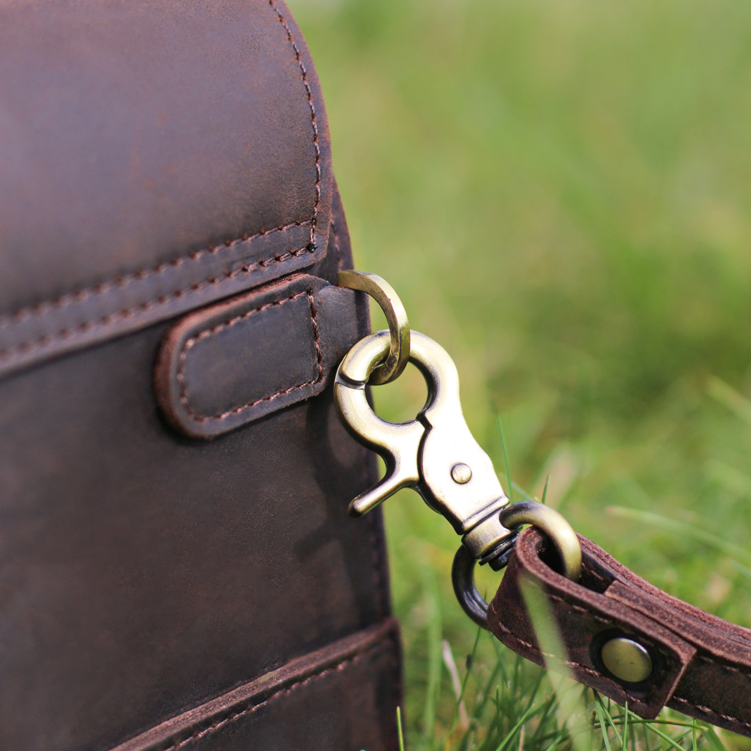 Close-up of a brass hook and leather loop on a dark brown clutch, emphasizing the high-quality materials and craftsmanship.