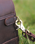 Close-up of a brass hook and leather loop on a dark brown clutch, emphasizing the high-quality materials and craftsmanship.