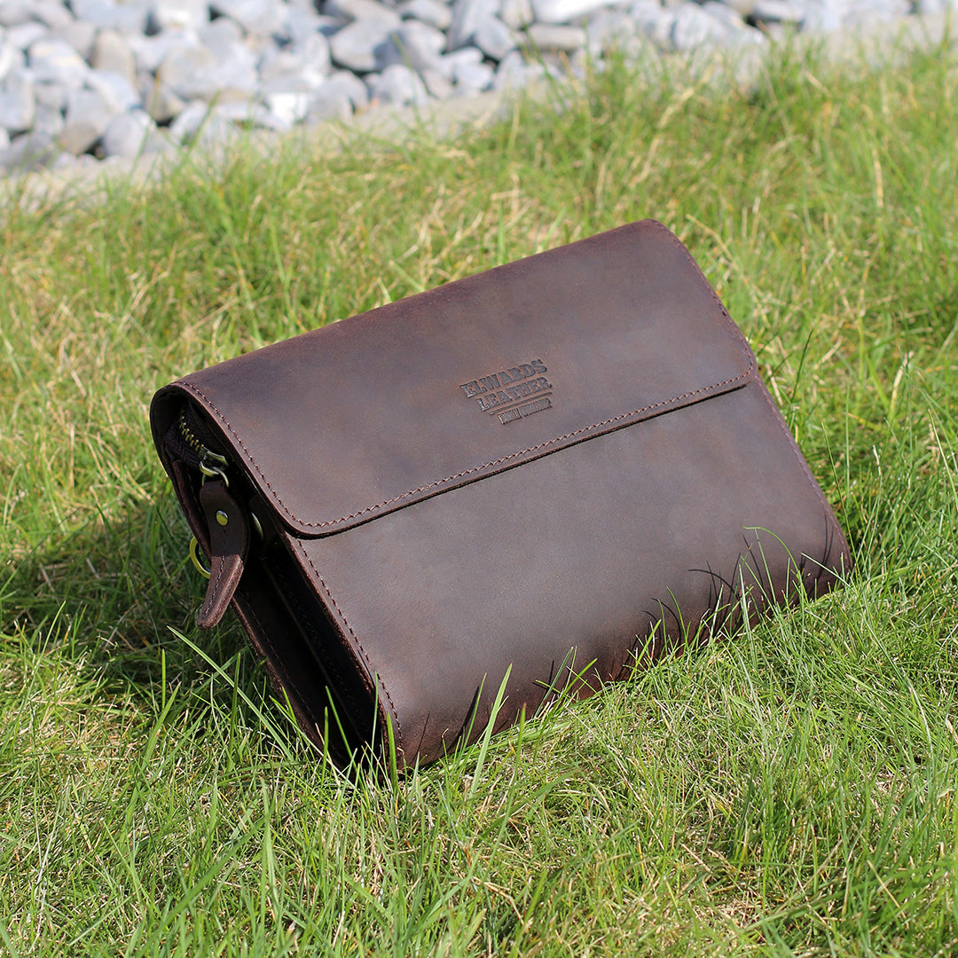 Dark brown leather clutch placed on grass, emphasizing its rugged yet elegant design and durable crazy horse leather.