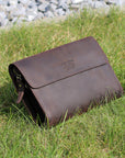 Dark brown leather clutch placed on grass, emphasizing its rugged yet elegant design and durable crazy horse leather.