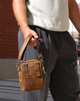 Person holding a brown leather crossbody bag outdoors.