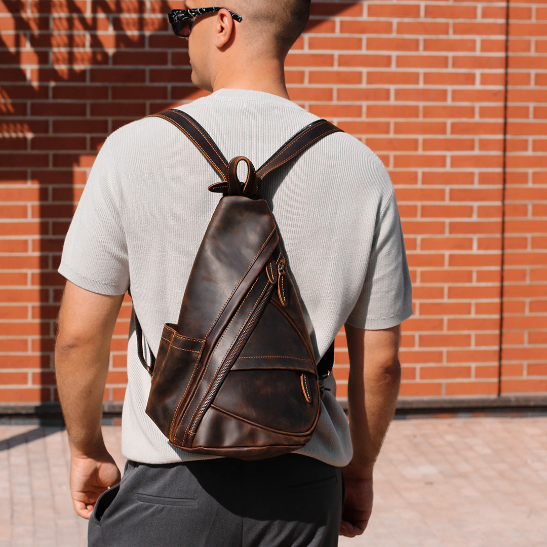 Man wearing a brown leather backpack against a brick wall.