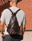 Man wearing a brown leather backpack against a brick wall.