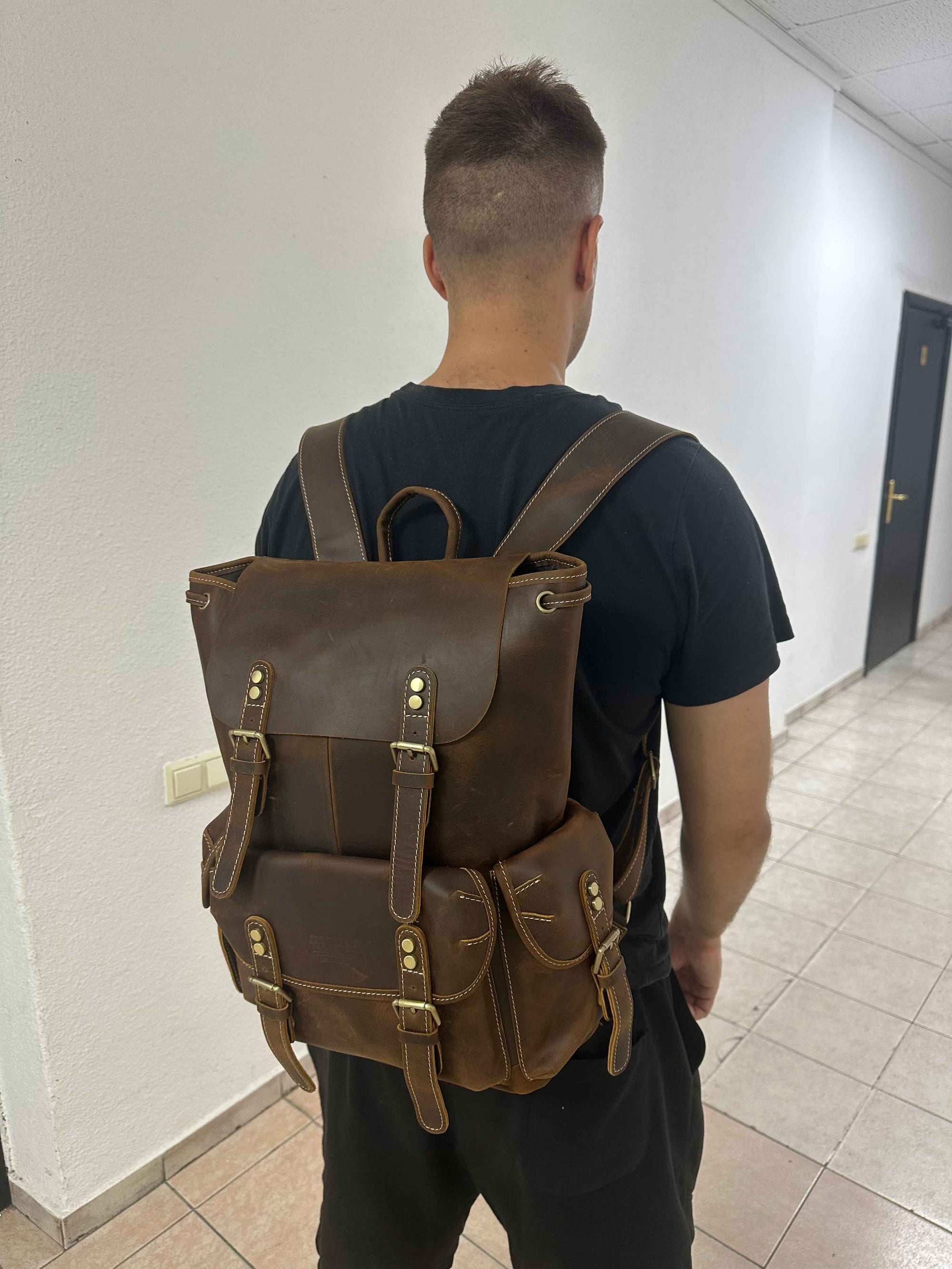 Man wearing a brown leather backpack indoors.