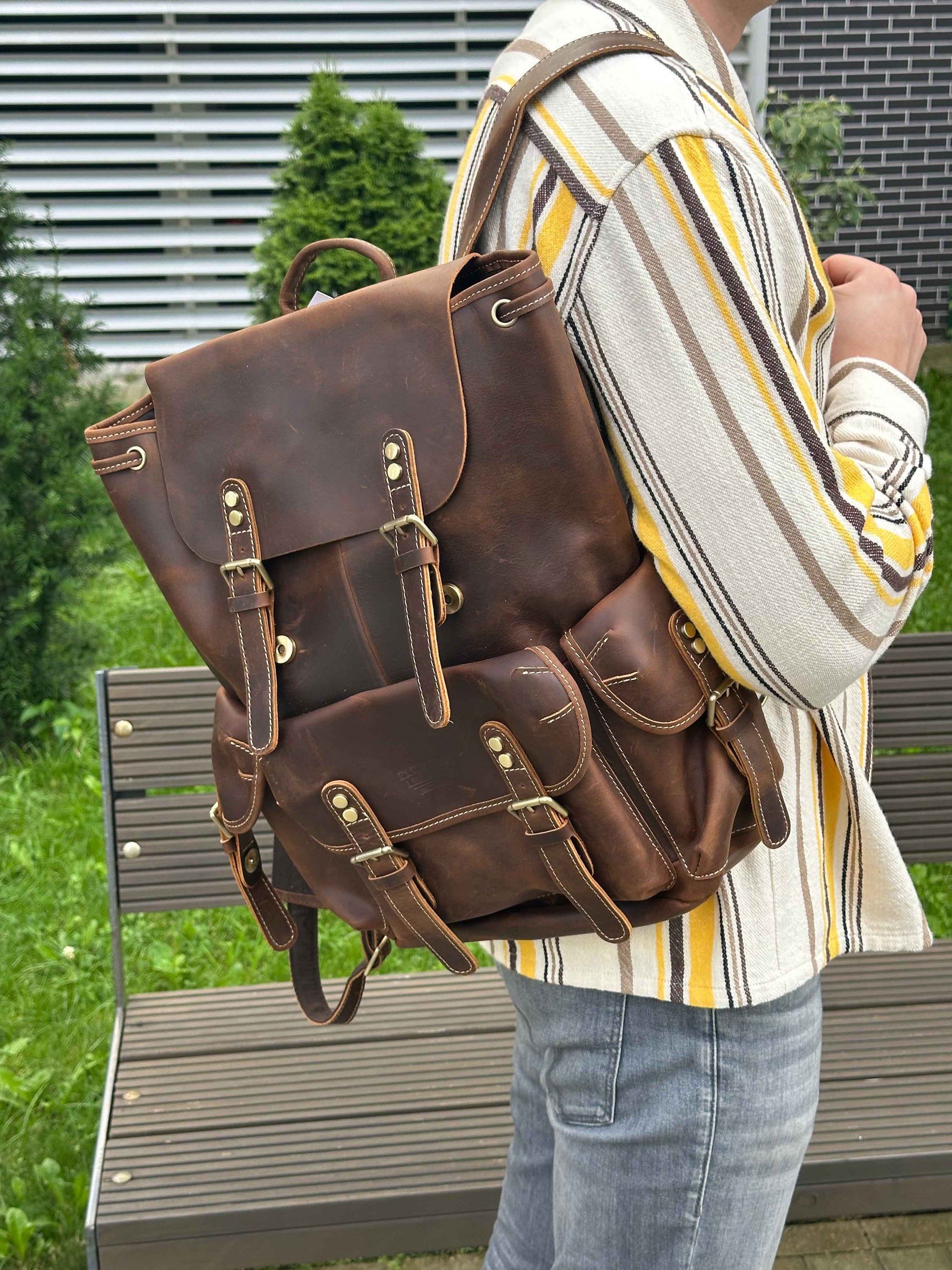 Person holding a brown leather backpack outdoors