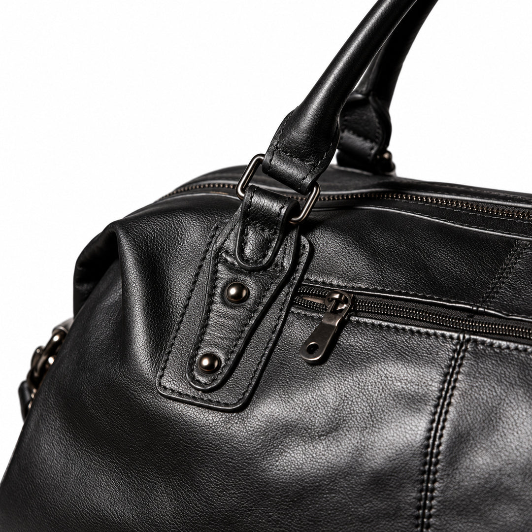 Elegant black full-grain leather duffel bag handle attachment with metal loop and twin rivets.