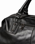 Elegant black full-grain leather duffel bag handle attachment with metal loop and twin rivets.