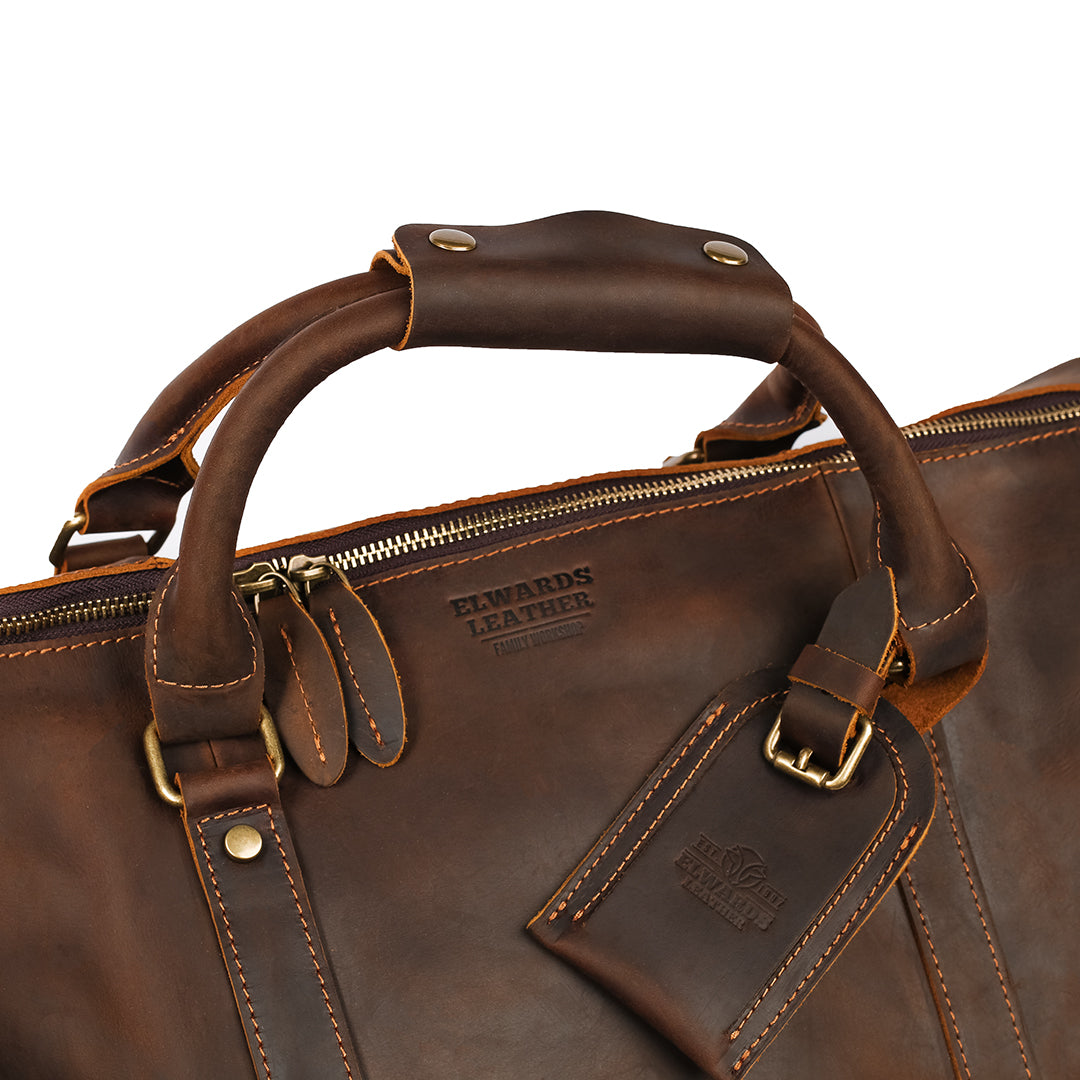 Close-up of Elwards Leather logo on premium leather duffle bag with reinforced handles and brass hardware.