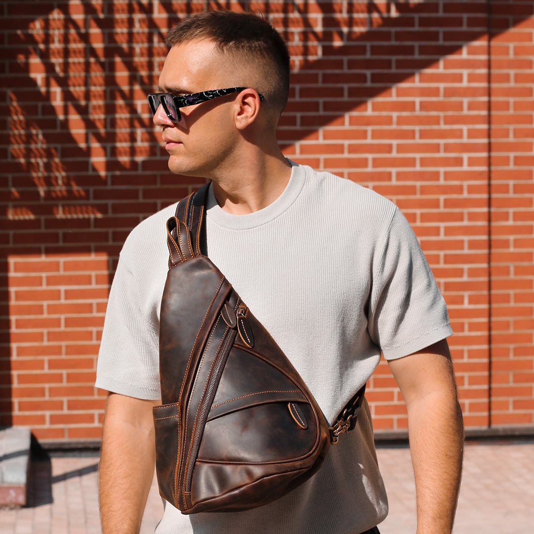 Man wearing a dark brown leather sling bag against a brick wall.