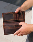 Brown leather wallet held open by a person's hands on a light background