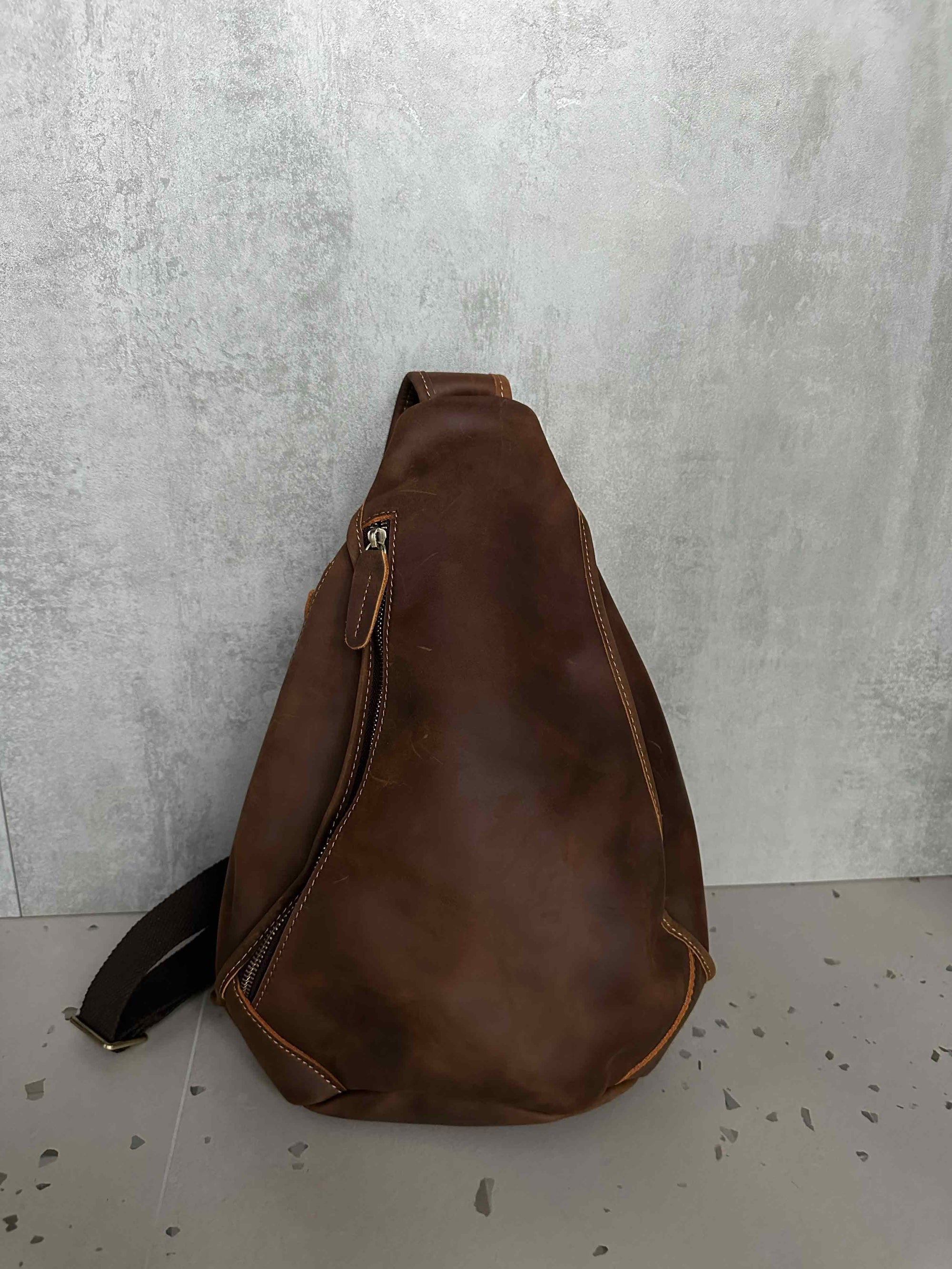 Brown leather sling bag on a light gray surface with a neutral background
