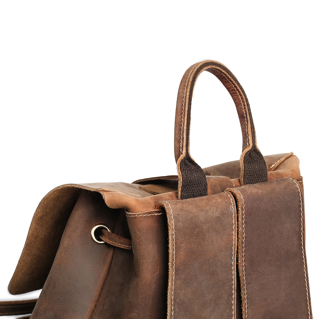 Close-up of the top handle and back straps of a vintage brown Crazy Horse leather backpack, highlighting stitching.