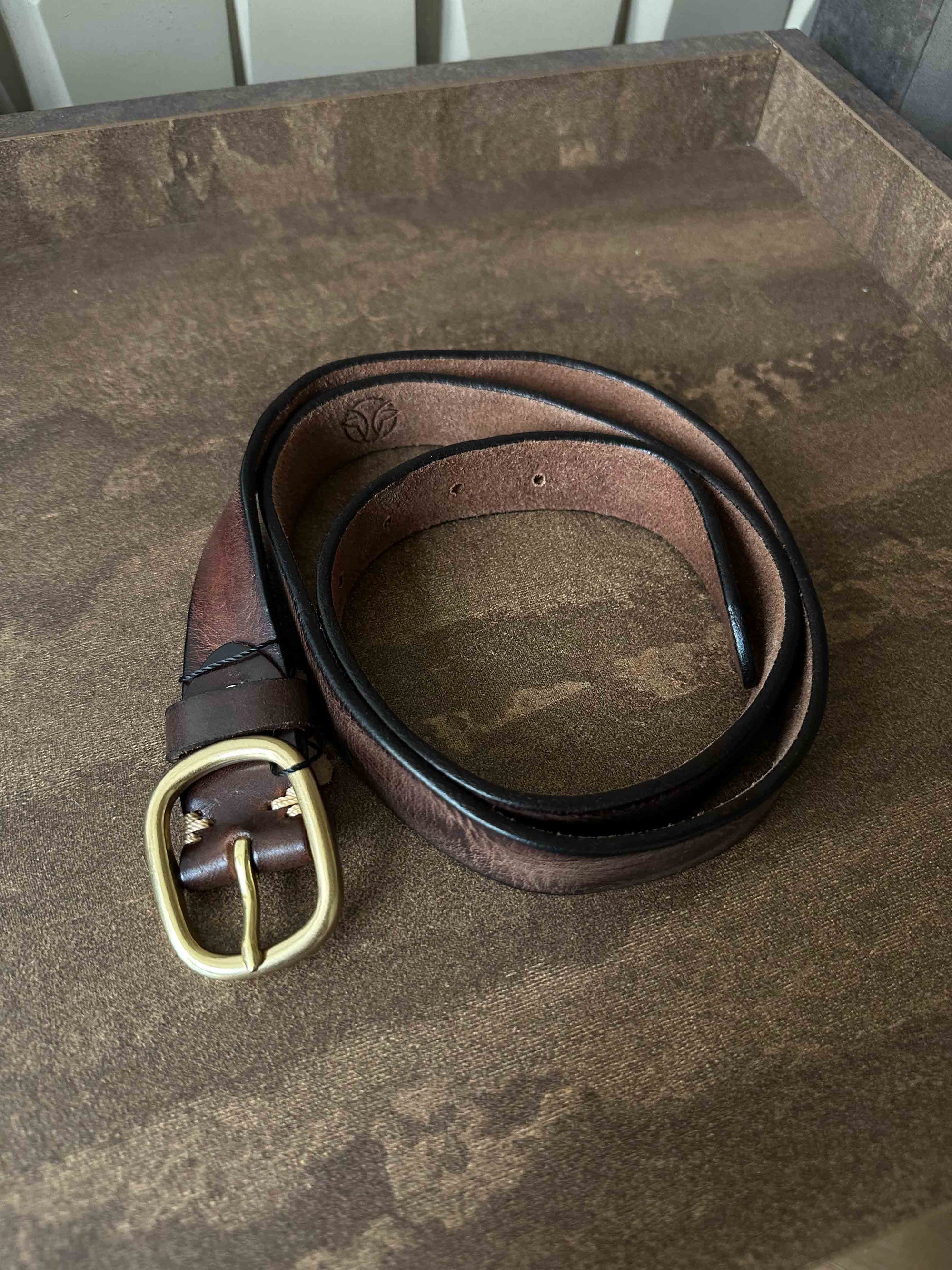 Brown leather belt with brass buckle on a brown textured surface