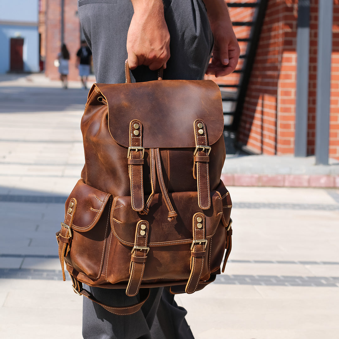 Brown leather backpack held by a person outdoors.