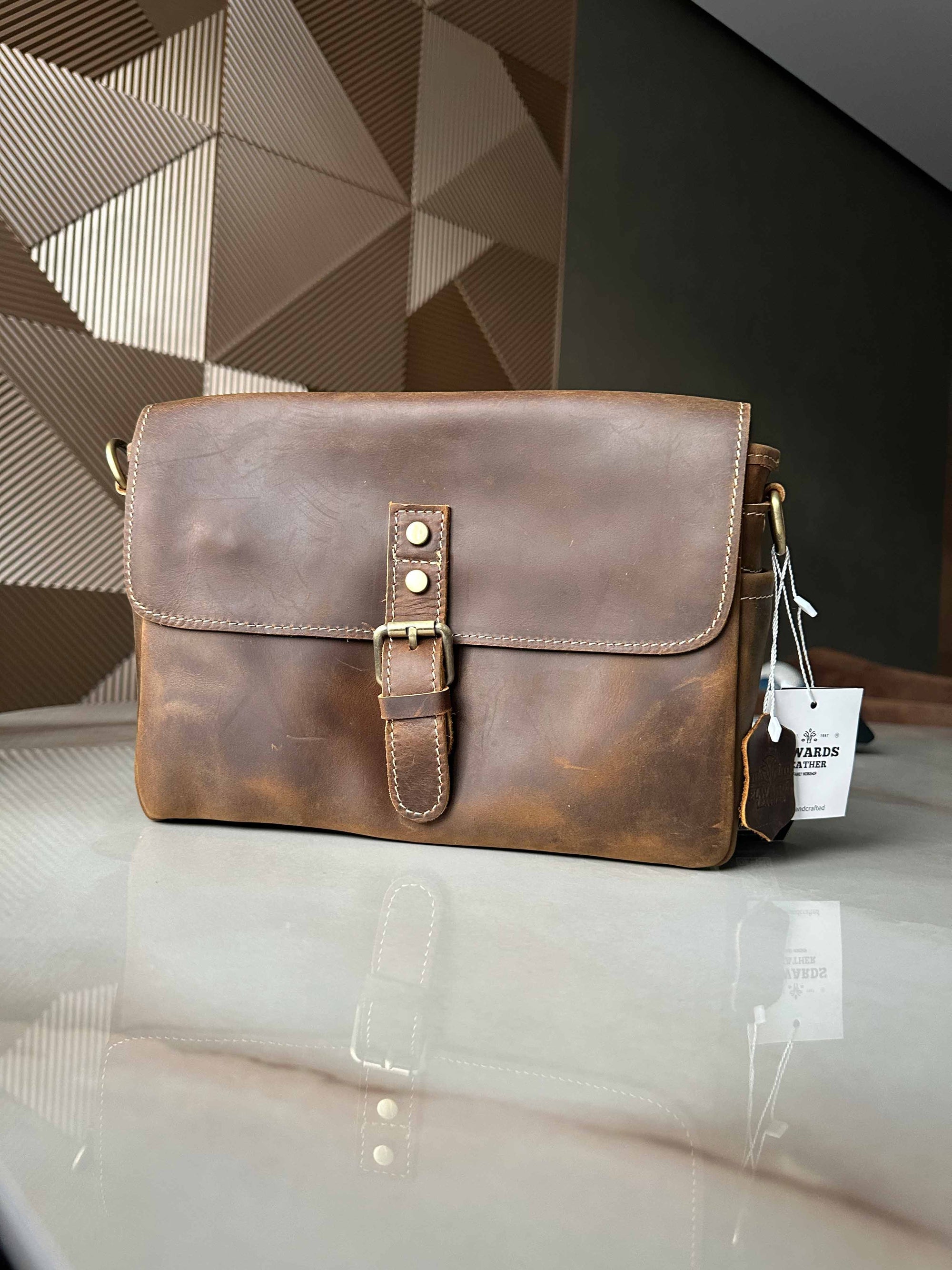 Brown leather bag with a tag on a reflective surface