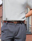 Person wearing a white shirt, gray pants, and a brown belt with a gold buckle.