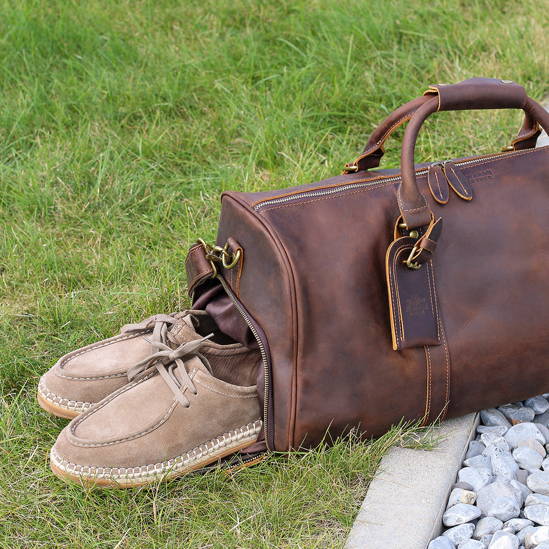 Handmade brown leather duffle bag with dedicated shoe compartment, shown outdoors with casual shoes partially stored.