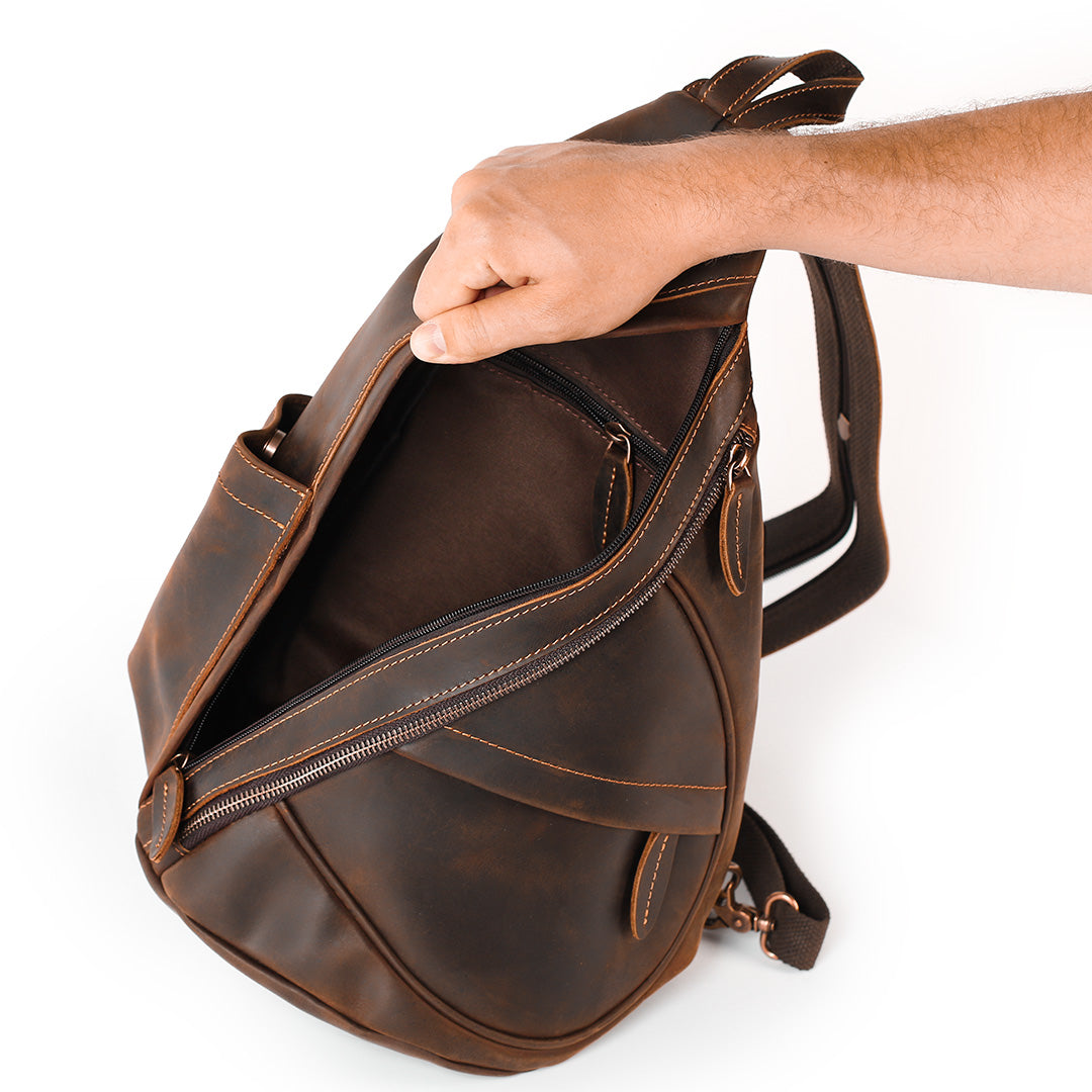 Brown leather backpack being held by a hand on a white background