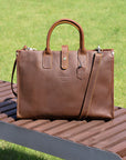 Handcrafted brown laptop leather briefcase resting on a bench in a sunny park.