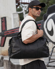 Large black leather overnight bag for men with dual handles, detachable shoulder strap and spacious weekender shape