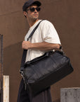 Large black leather travel duffle bag for men with reinforced carry handles, shoulder strap and structured base