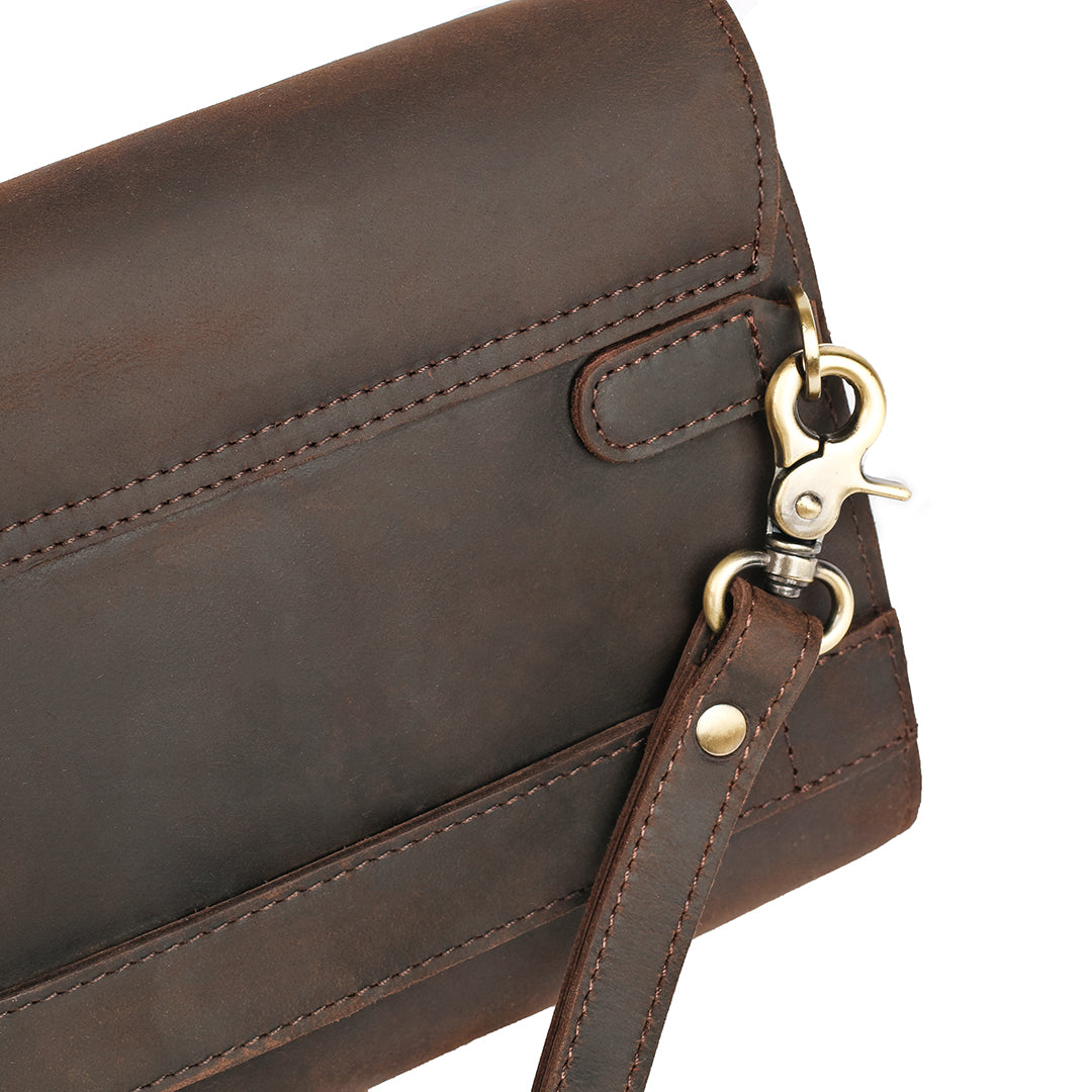 Close-up of a brass hook and leather strap on the back of a dark brown clutch, showcasing durability and premium hardware.