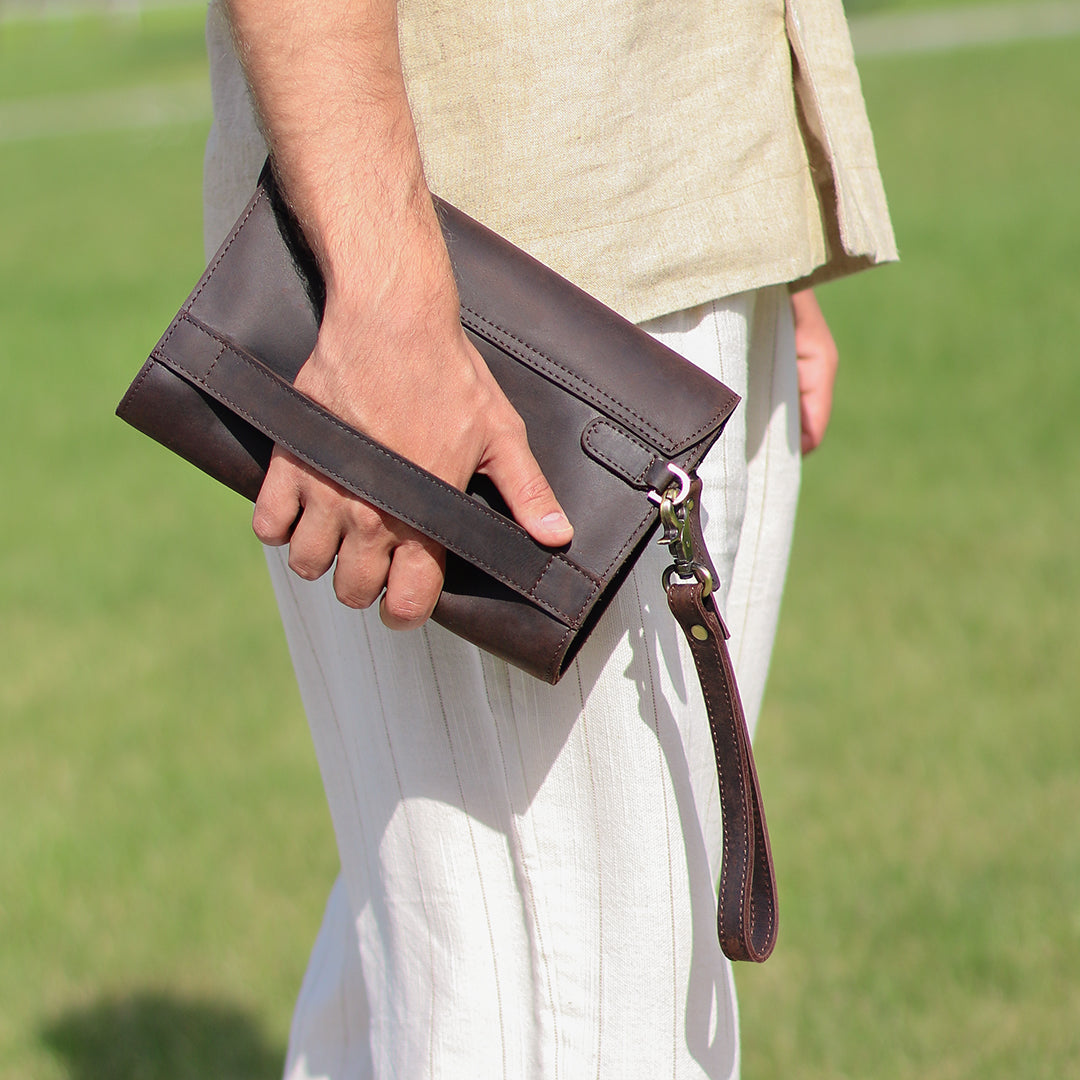 Side view of a men&#39;s dark brown clutch being held by its sturdy grip strap, illustrating its ergonomic and functional design.