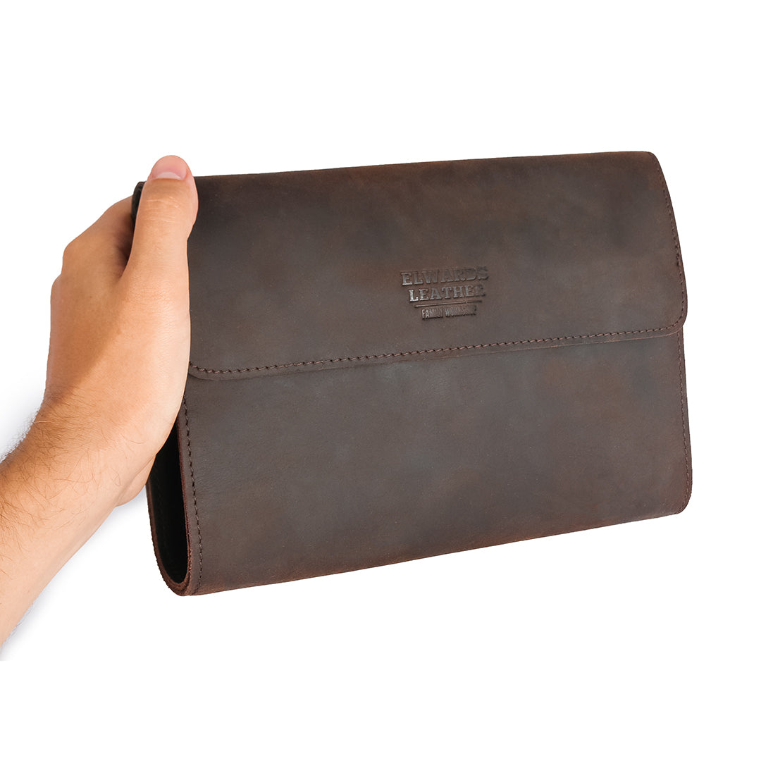 Men&#39;s hand holding a handmade dark brown leather clutch, illustrating its compact size and practical design for everyday use.