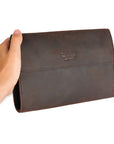 Men's hand holding a handmade dark brown leather clutch, illustrating its compact size and practical design for everyday use.